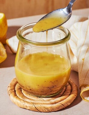 a close up of dijon vinaigrette in a glass jar, with a bit being lifted out with a spoon.