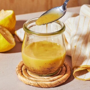 a close up of dijon vinaigrette in a glass jar, with a bit being lifted out with a spoon.