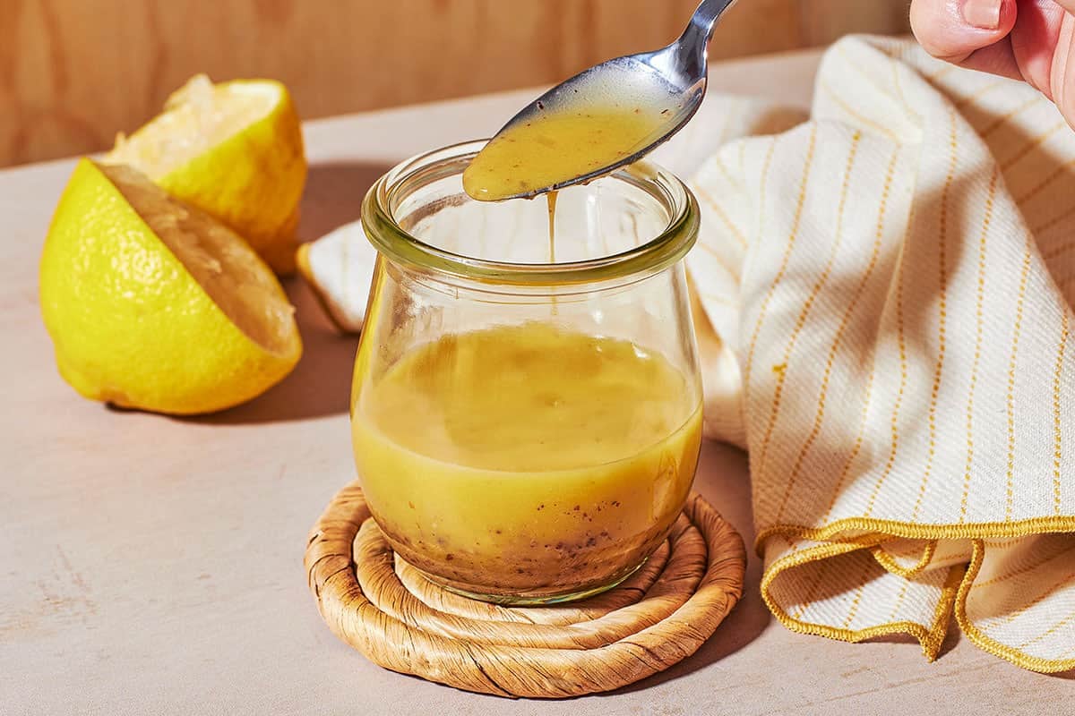 a close up of dijon vinaigrette in a glass jar, with a bit being lifted out with a spoon.