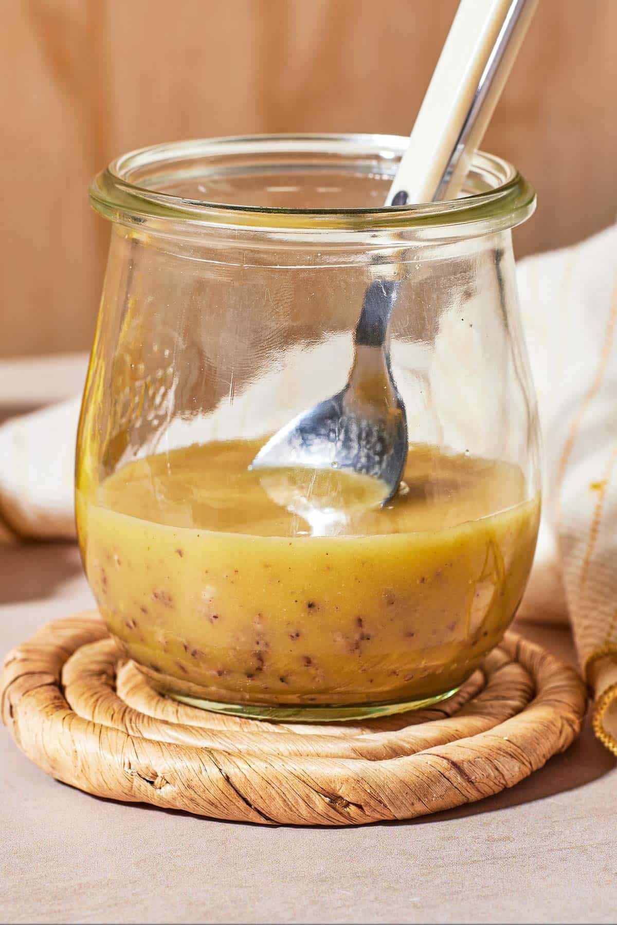 a close up of dijon vinaigrette in a glass jar with a spoon.