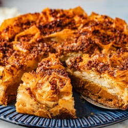 a close up of a baked baklava pumpkin pie with two slices cut into it, one being lifted out with a pie server.