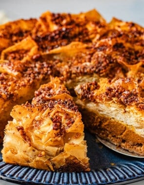 a close up of a baked baklava pumpkin pie with two slices cut into it, one being lifted out with a pie server.