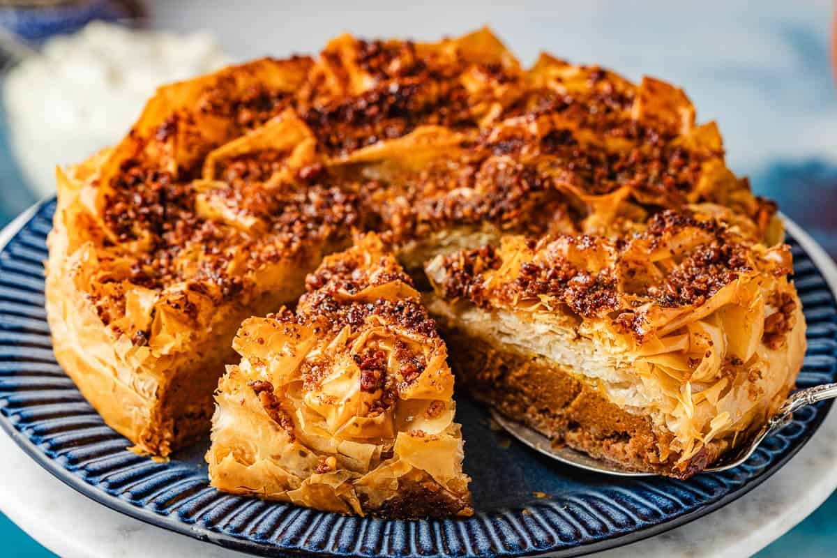 a close up of a baked baklava pumpkin pie with two slices cut into it, one being lifted out with a pie server.