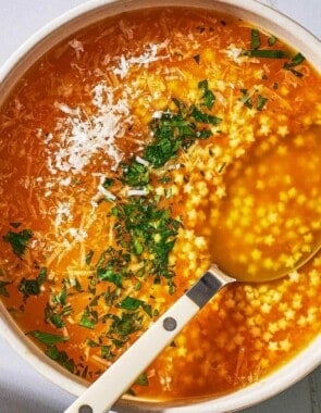 an overhead photo of a serving of pastina soup garnished with parsley and parmesan cheese in a bowl with a spoon.