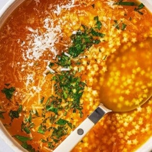 an overhead photo of a serving of pastina soup garnished with parsley and parmesan cheese in a bowl with a spoon.