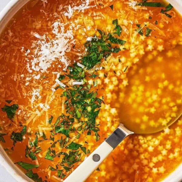 an overhead photo of a serving of pastina soup garnished with parsley and parmesan cheese in a bowl with a spoon.