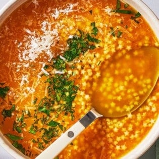 an overhead photo of a serving of pastina soup garnished with parsley and parmesan cheese in a bowl with a spoon.