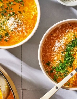 an overhead photo of 2 bowls of pastina soup garnished with parsley and parmesan cheese, one with a spoon, next to a pot of soup with a ladle.