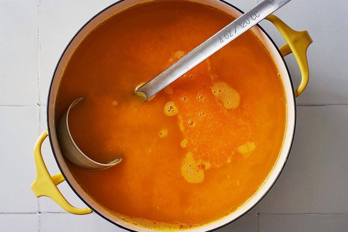 an overhead photo of the blended vegetables and broth in a pot with a ladle.