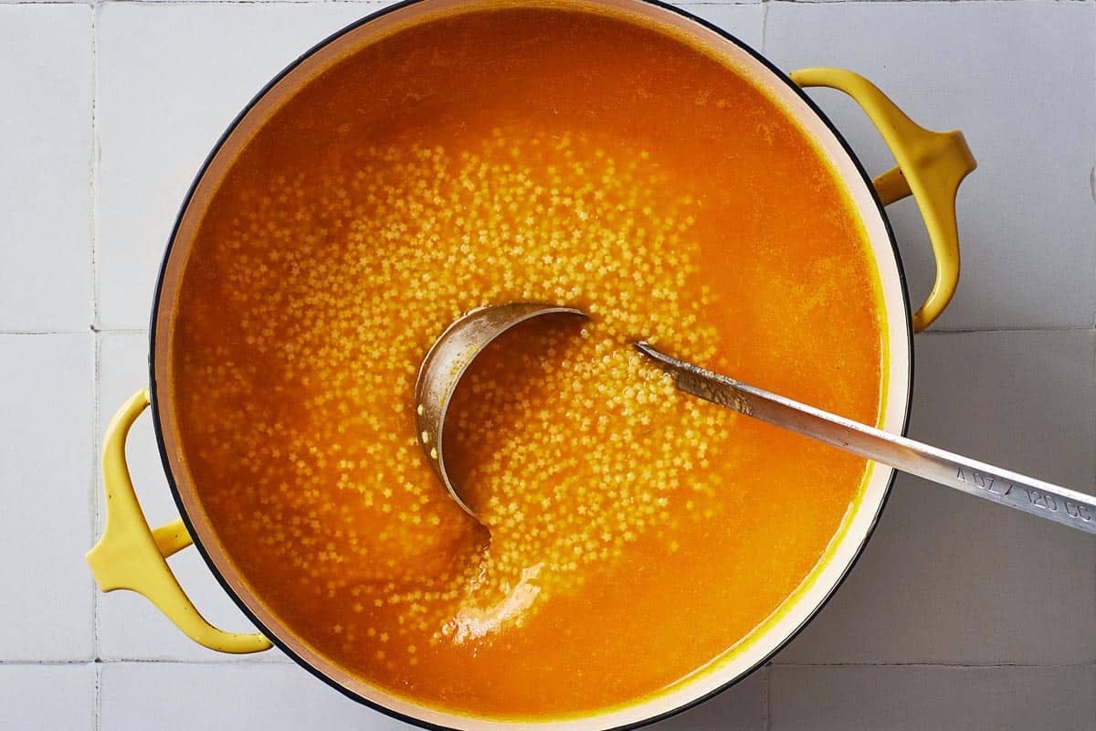 an overhead photo of a pot of pastina soup with a ladle.