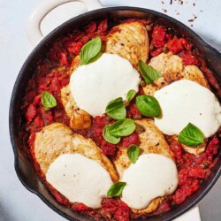 pollo alla pizzaiola chicken in tomato sauce in a skillet next to a small bowl of red pepper flakes.