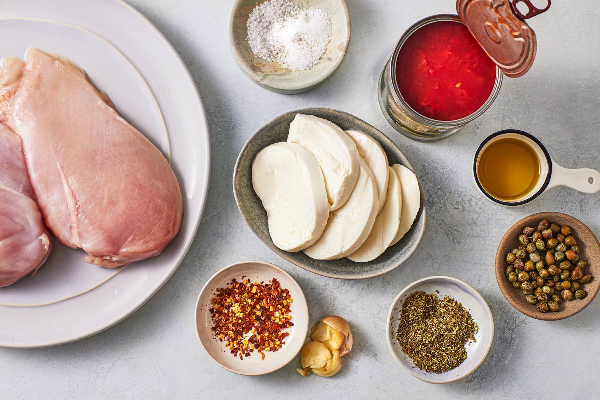 ingredients for pollo alla pizzaiola chicken in tomato sauce including chicken mozzarella cheese, olive oil, garlic, canned diced tomatoes, capers, salt, red pepper flakes, and Italian seasoning.