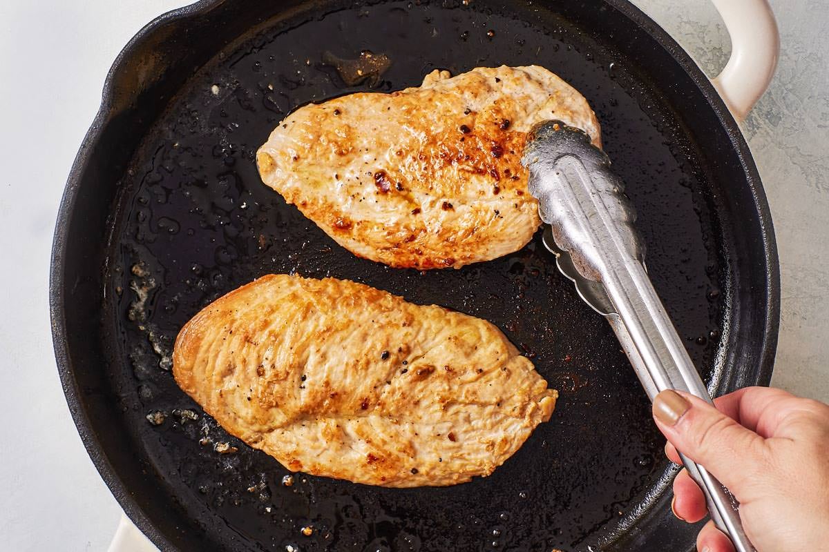 two chicken cutlets being browned in a skillet.
