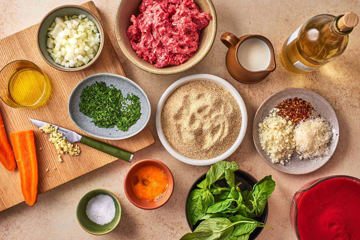 ingredients for polpette including ground beef, breadcrumbs, milk, parsley, garlic, egg, parmesan cheese, pecorinao romano cheese, white wine, salk, olive oil, onion, tomato passata, red pepper flakes, carrots, and basil.