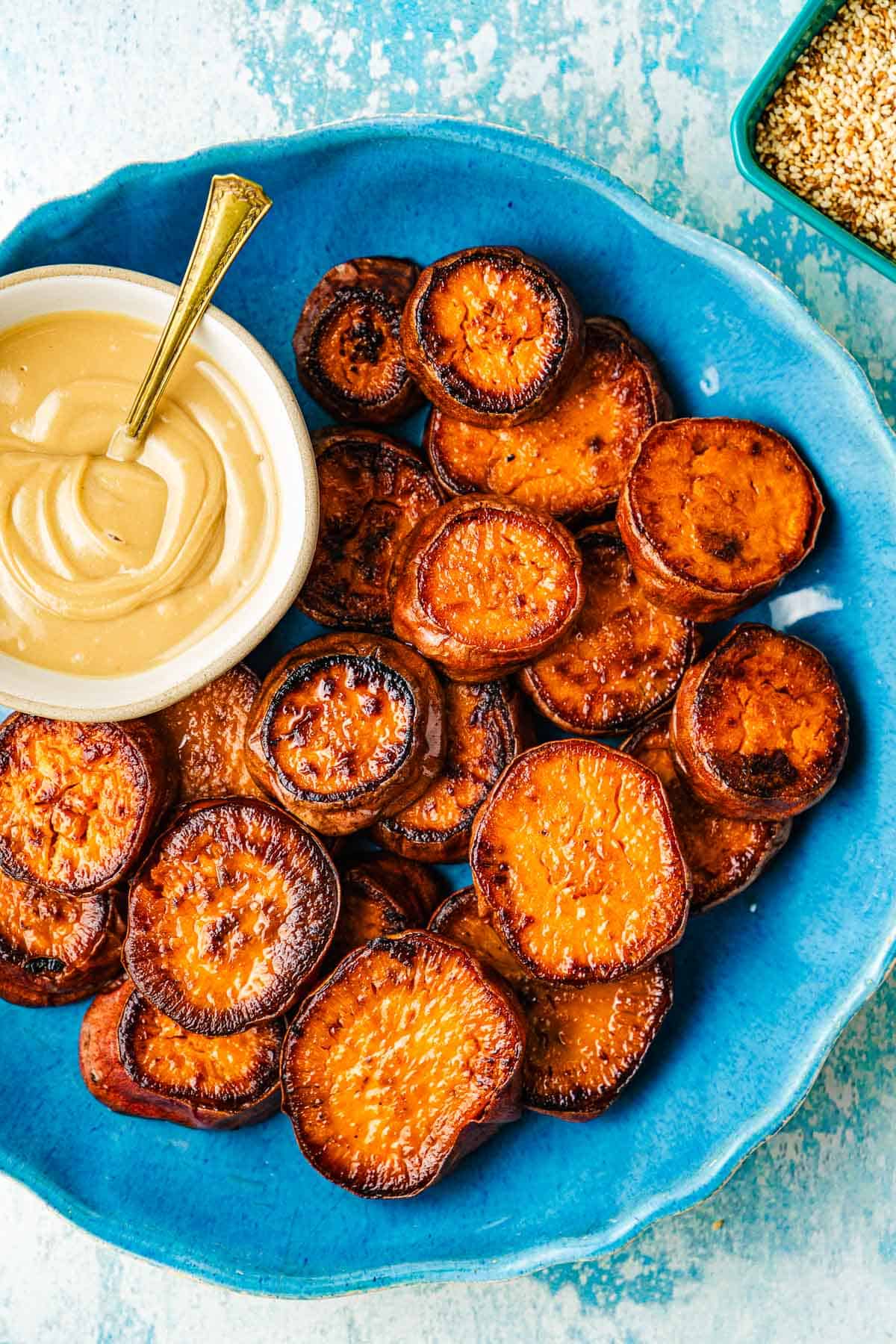 Roasted sweet potatoes on a blue shallow bowl with a white bowl of honeyed tahini on the side.