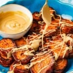 A spoon drizzling honeyed tahini over roasted sweet potatoes, showing its thick and sticky caramel-like consistency.