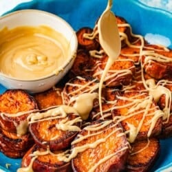 A spoon drizzling honeyed tahini over roasted sweet potatoes, showing its thick and sticky caramel-like consistency.