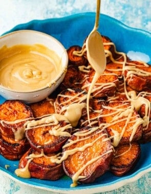 A spoon drizzling honeyed tahini over roasted sweet potatoes, showing its thick and sticky caramel-like consistency.