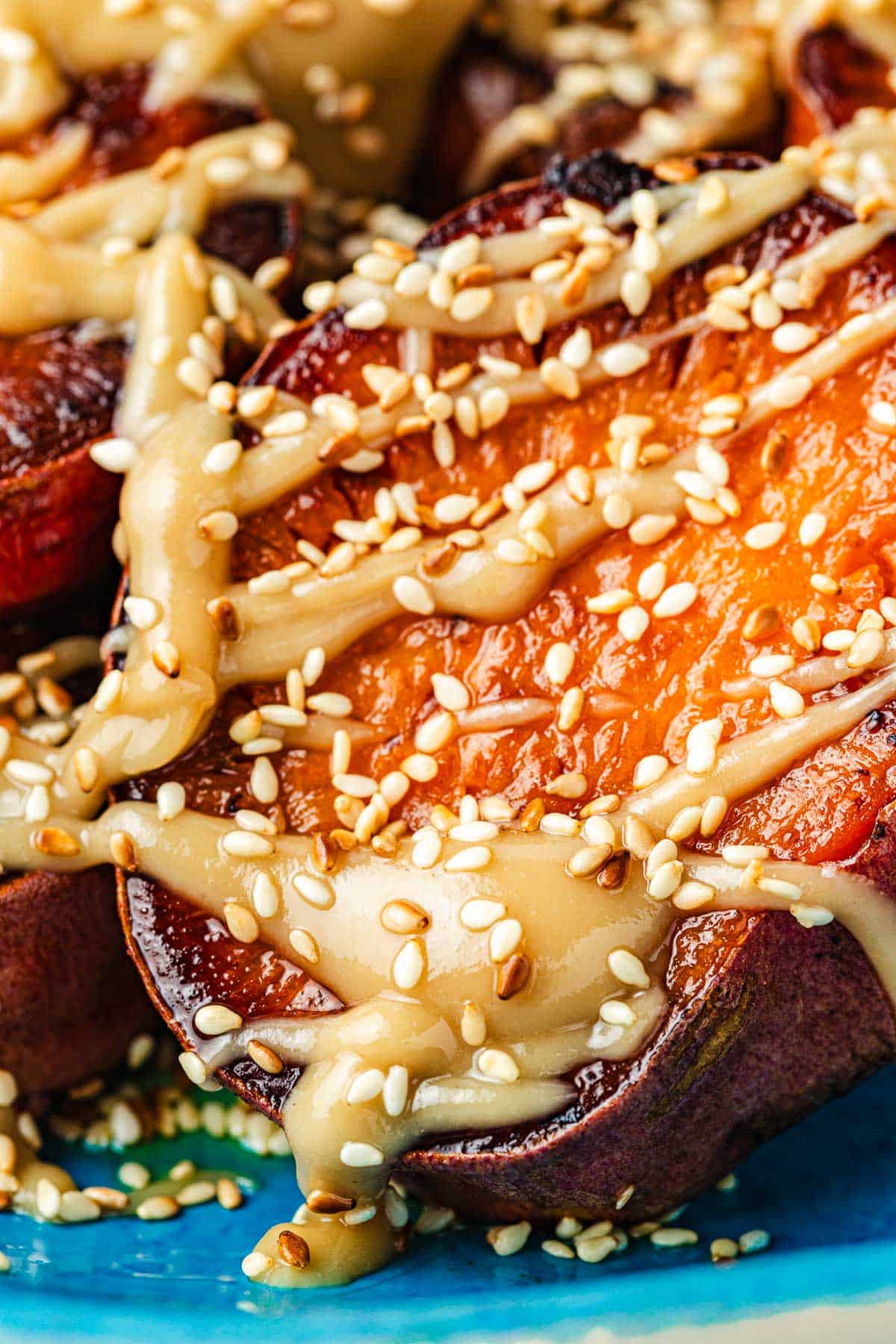 Close up shot of a roasted sweet potato with a drizzle of honeyed tahini and a sprinkling of sesame seeds.