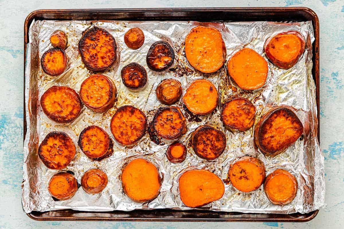 Roasted sweet potatoes on a sheet pan. Half are flipped showing the browned bottom and slightly charred edges.