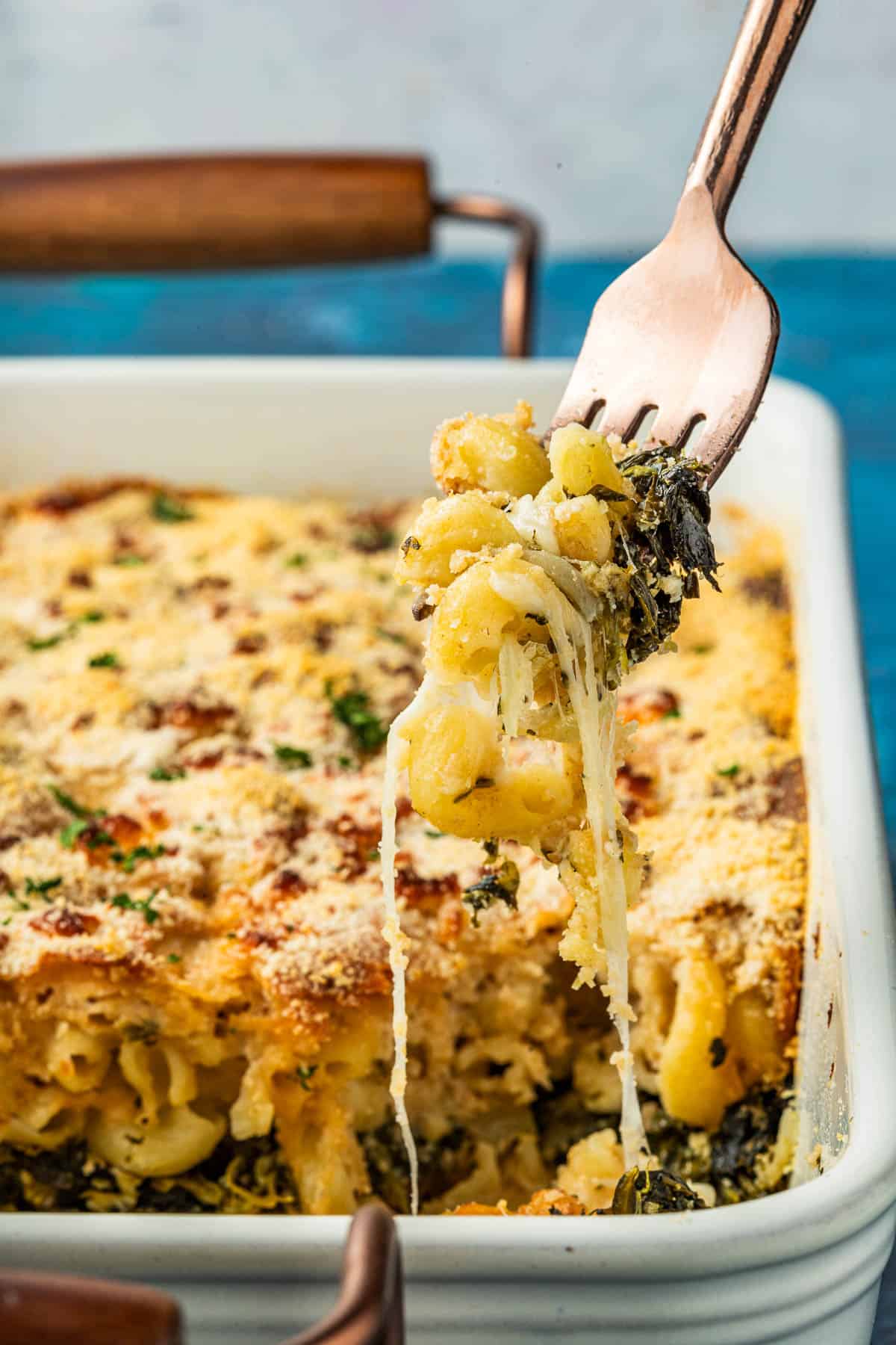 Fork pulling up a bite of Spanakopita Mac and cheese, showing the crispy breadcrumbs and melted cheese pulling from the casserole.