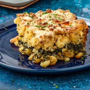 Corner piece that has been cut out of Spanakopita Mac and cheese, showing the layer of spinach, onion, and herb mixture in the center and the golden brown curst.