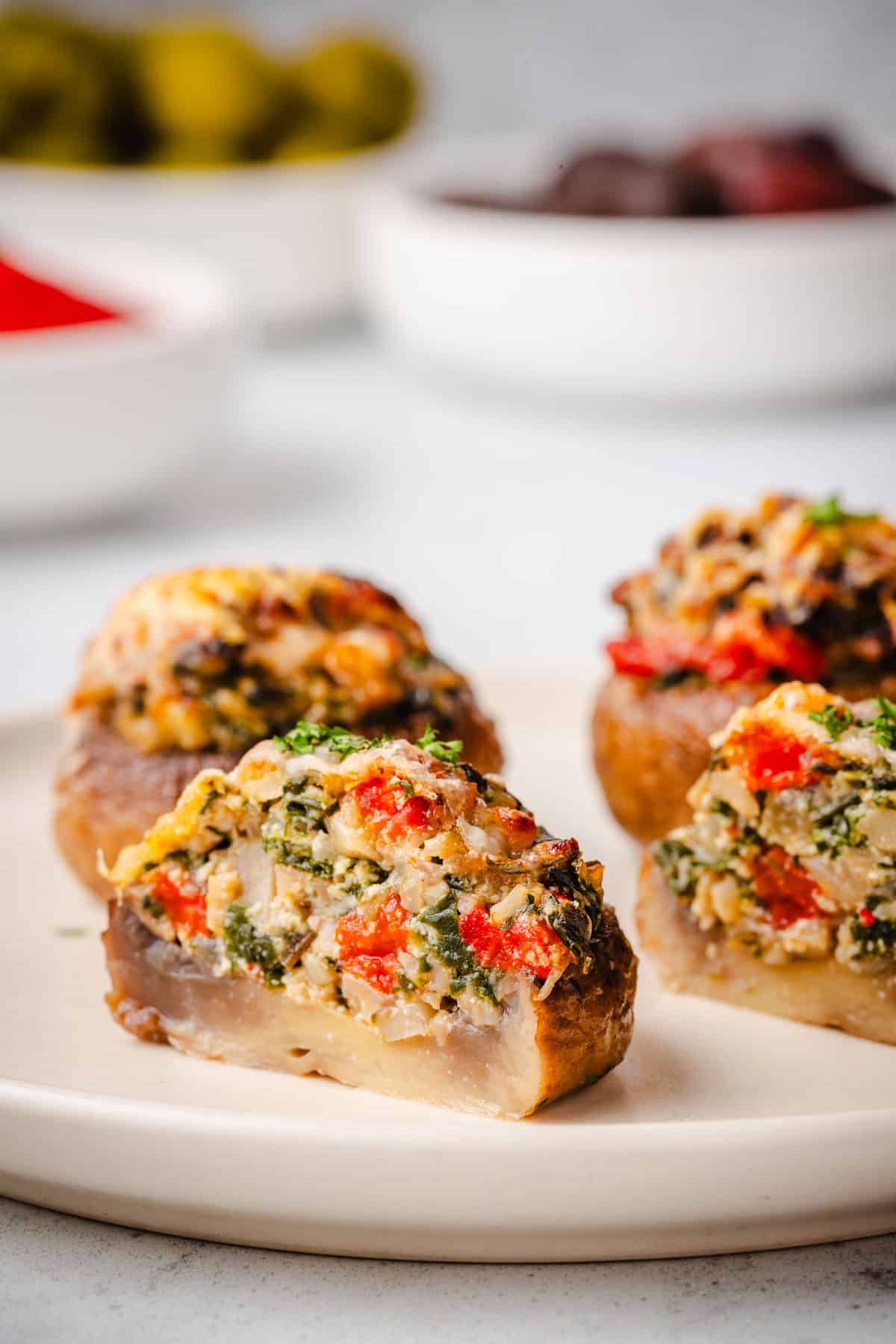 a close up of a stuffed mushroom cut in half in front of two whole stuffed mushrooms on a plate.