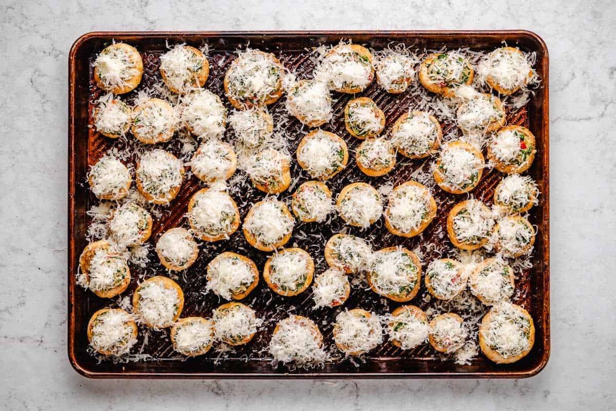 several uncooked stuffed mushrooms topped with parmesan cheese on a baking sheet.