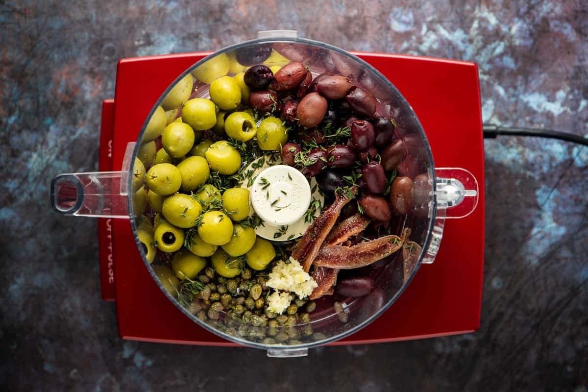 the ingredients for olive tapenade in the bowl of a food processor before being mixed.