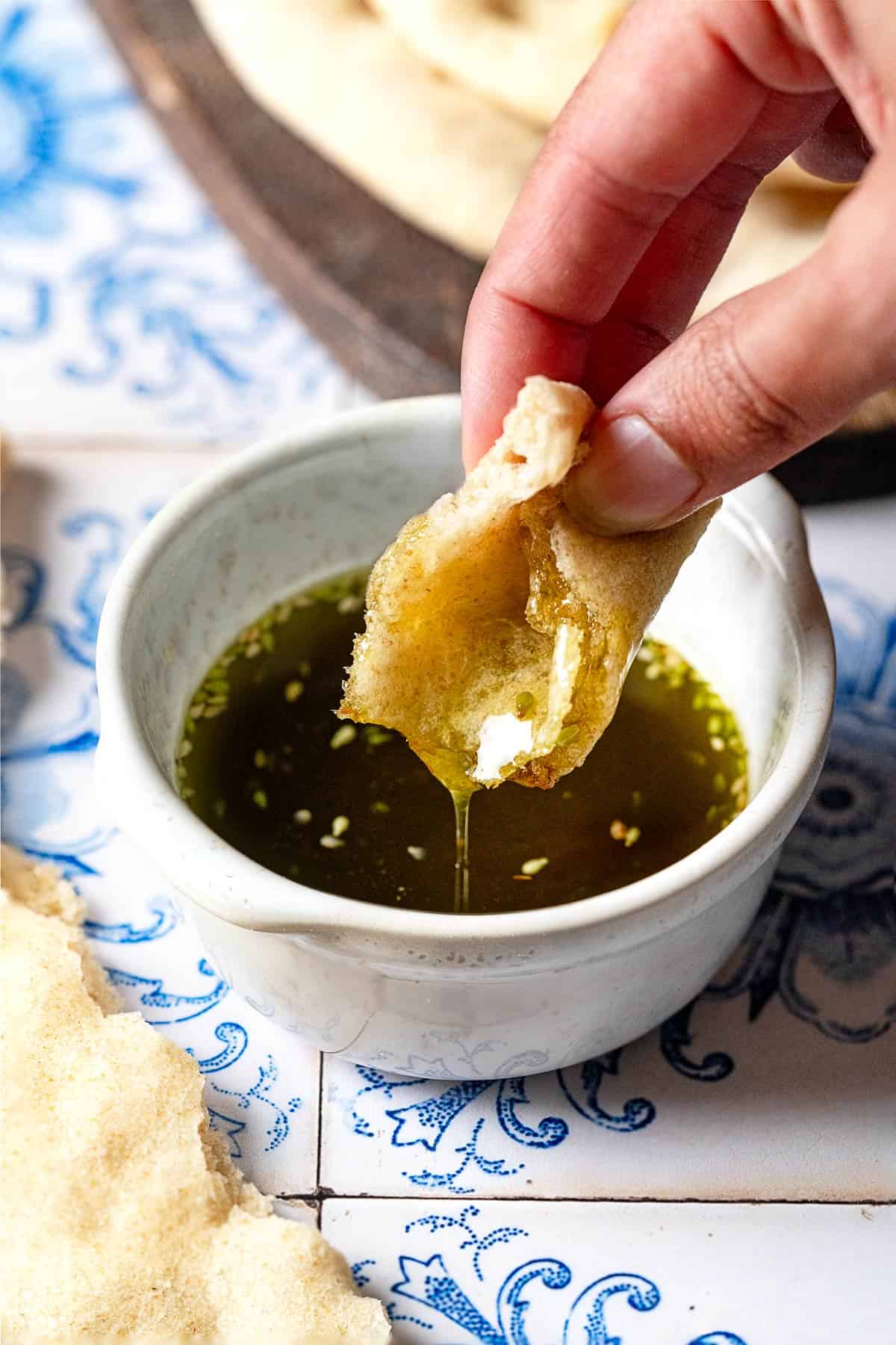 a piece of taboon flatbread being dipped into seasoned olive oil.