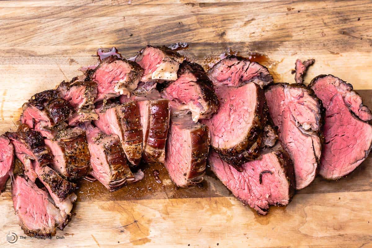 slices of roasted beef tenderloin on a wooden surface.