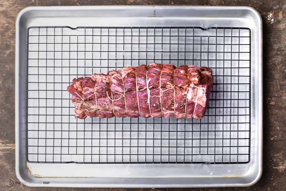 a seasoned and trussed beef tenderloin on a wire rack sitting in a sheet pan.