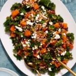 butternut squash salad on a serving platter with gold serving utensils.