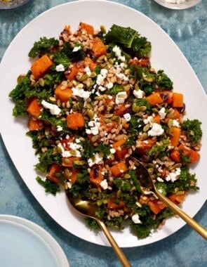 butternut squash salad on a serving platter with gold serving utensils.