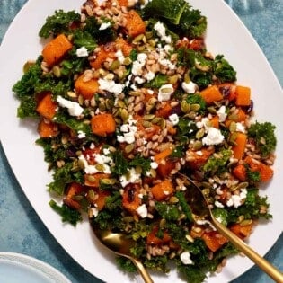 butternut squash salad on a serving platter with gold serving utensils.