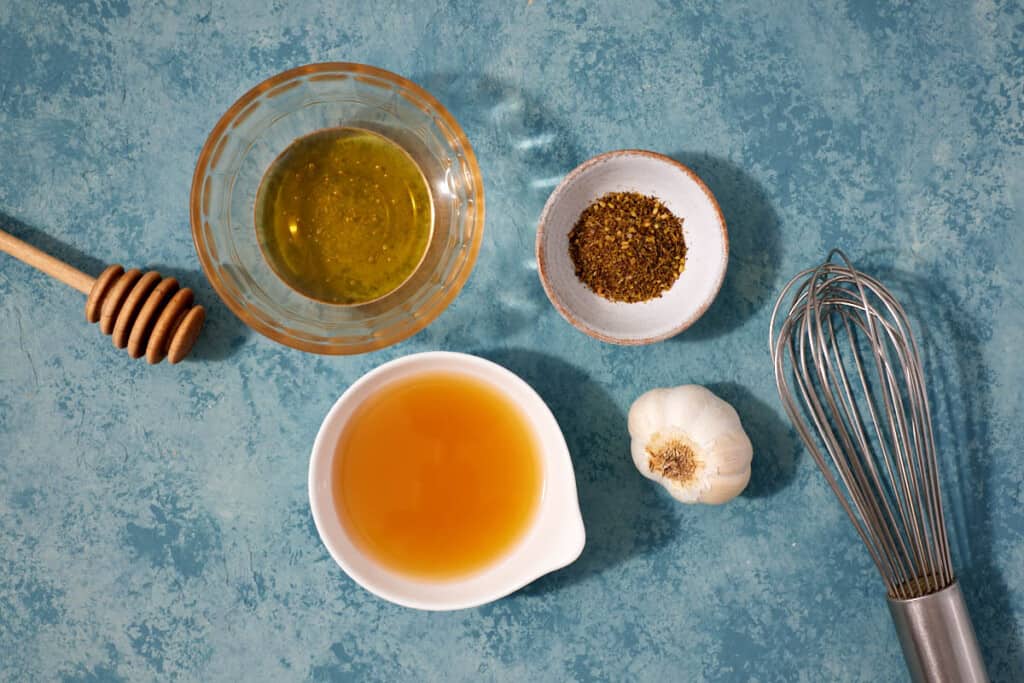 ingredients for the butternut squash salad dressing including olive oil, apple cider vinegar, garlic, za'atar, and honey.