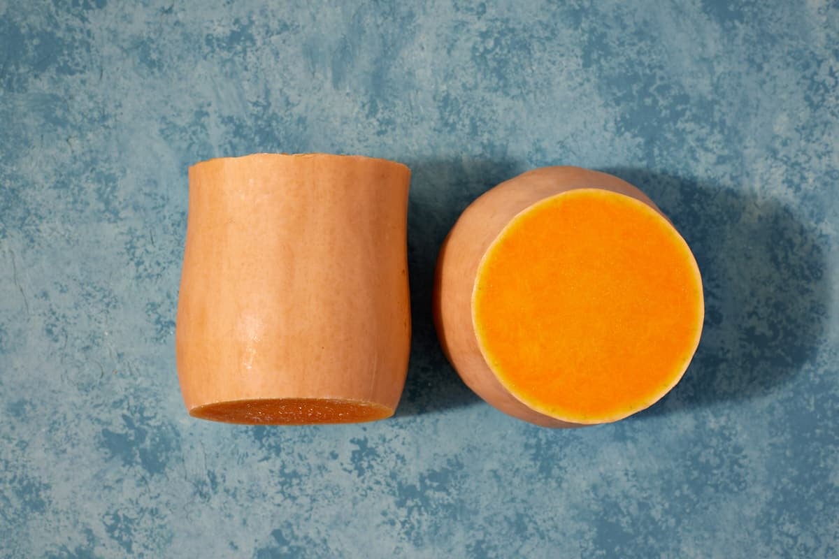 two butternut squash halves next to each other, one laying on it's side, and one sitting upright, exposing the inner flesh.