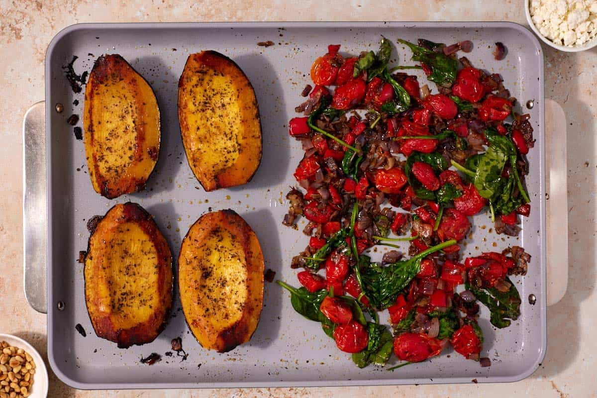 Roast acorn squash on one side and the tomato mixture on the other, showing the wilted spinach that's darker in color and reduced in size.