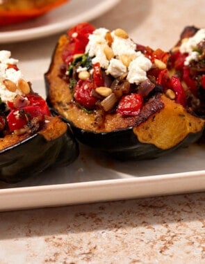 Side shot of three roasted acorn squash quarters stuffed with spinach, onions, and tomatoes and topped with goat cheese and pine nuts.