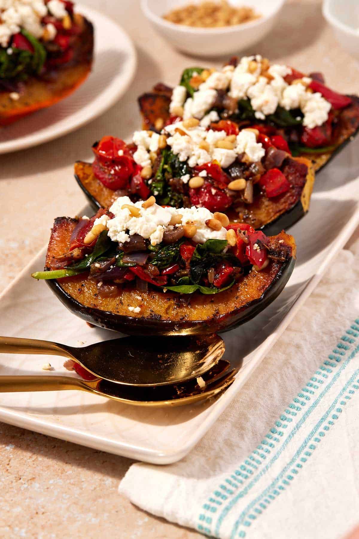 Three stuffed acorn squash quarters on a serving platter with large spoons.