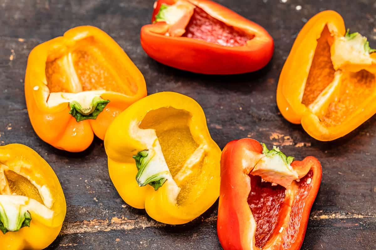 6 hollowed out red, yellow and orange bell pepper halves on a table.