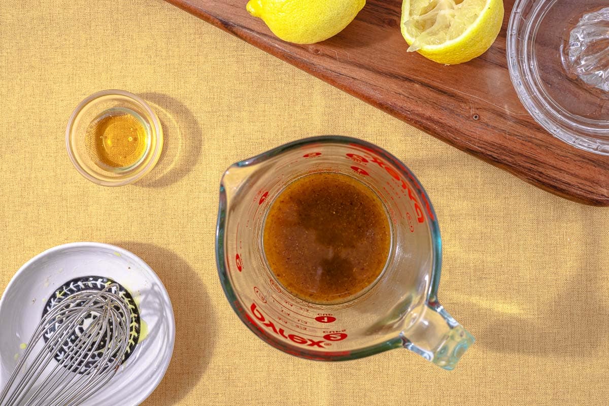 overhead shot of a measuring cup showing lemon juice, honey, garlic powder, sumac, salt, pepper, and olive oil after it has been whisked together.