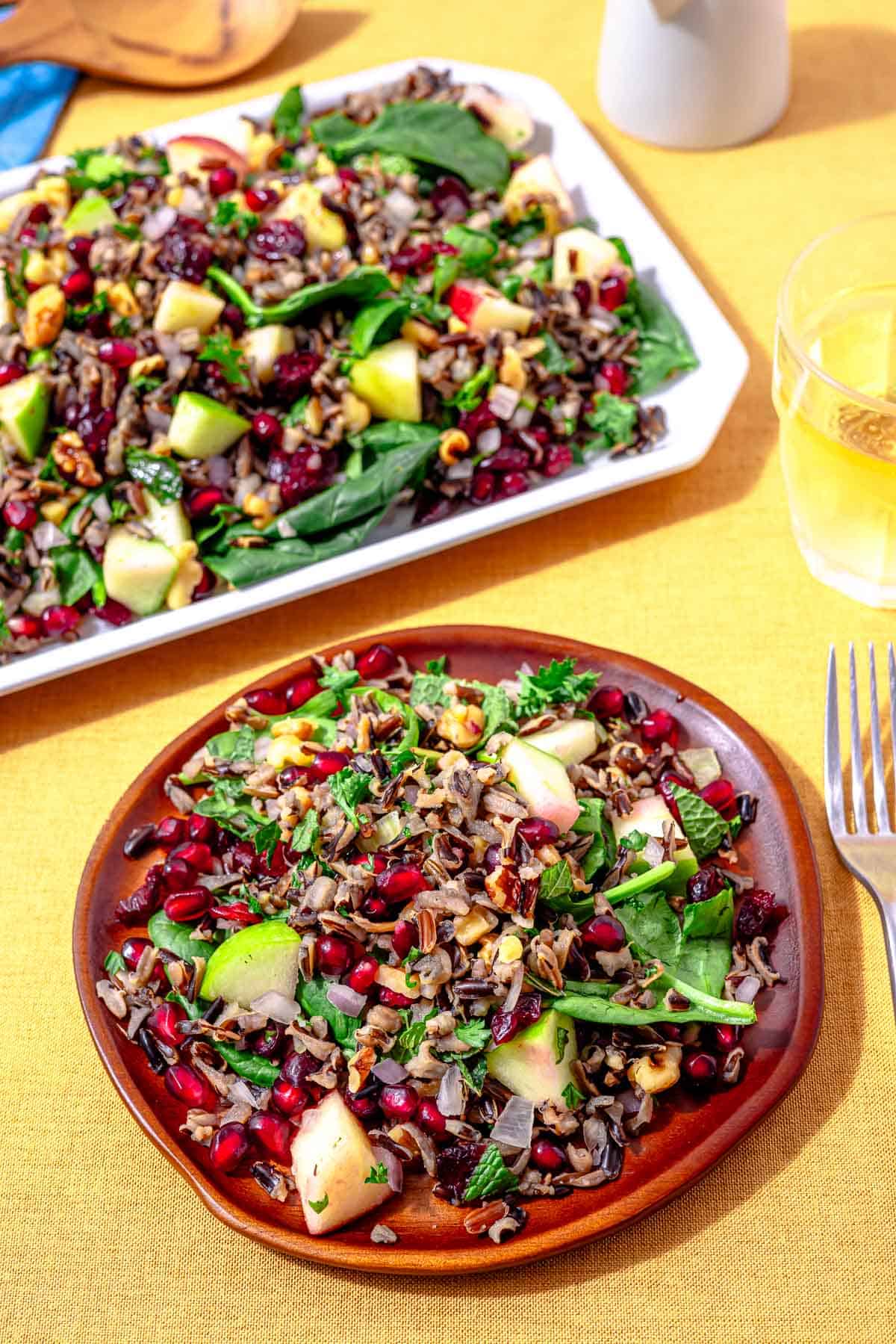 serving of wild rice salad on a plate with a fork and the large platter of salad in the background.