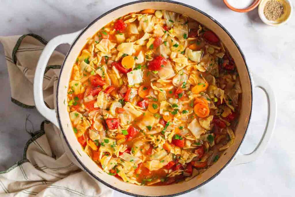 an overhead photo of a pot of detox cabbage soup surrounded by small bowls of salt and pepper and a cloth napkin.