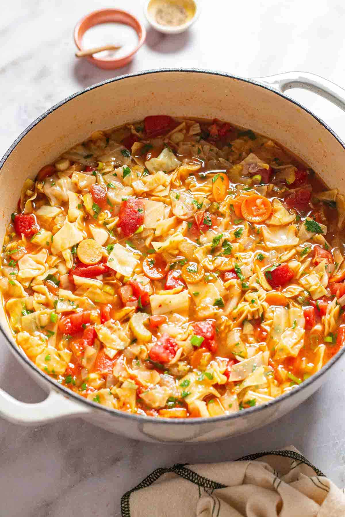 a pot of detox cabbage soup surrounded by small bowls of salt and pepper and a cloth napkin.