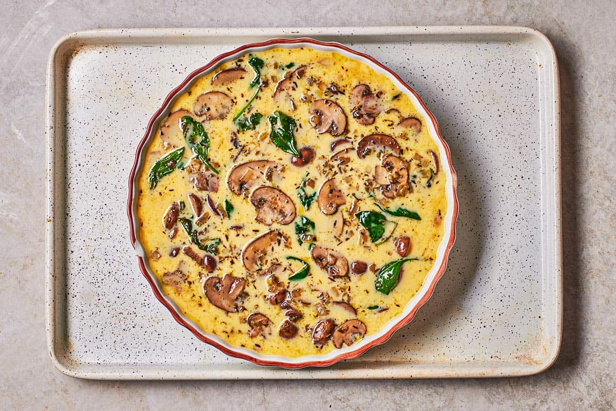 an unbaked crustless quiche in a pie plate on a sheet pan.