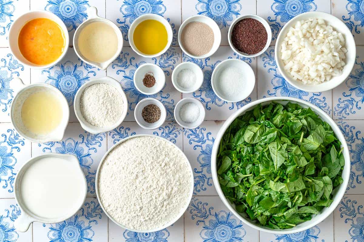 Ingredients for Fatayer Spinach and Onion Hand Pies including flour, sugar, milk, yeast, grape seed oil, spinach, salt, olive oil, chopped onion, sumac, pepper, allspice, lemon juice, and 1 beaten egg.