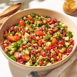 a close up of vegan chickpea salad in a serving bowl next to a wooden serving spoon and fork, a jar of dijon dressing, and a cloth napkin.