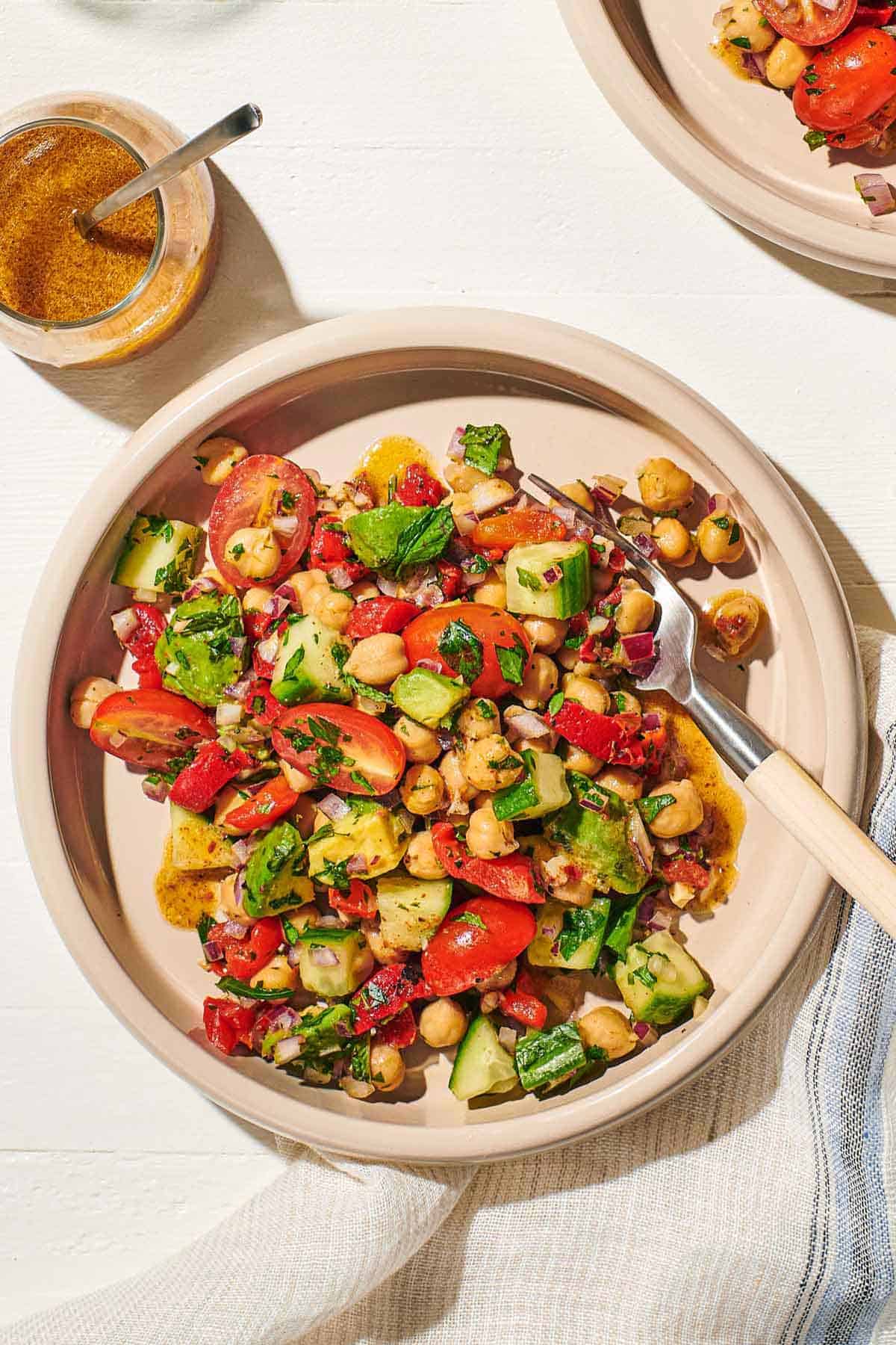 an overhead photo of a bowl of vegan chickpea salad with a fork next to a jar of dijon dressing, and a cloth napkin.