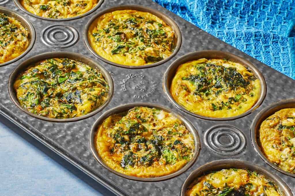 Spanakopita egg muffins in a muffin tin, showing the golden edges.